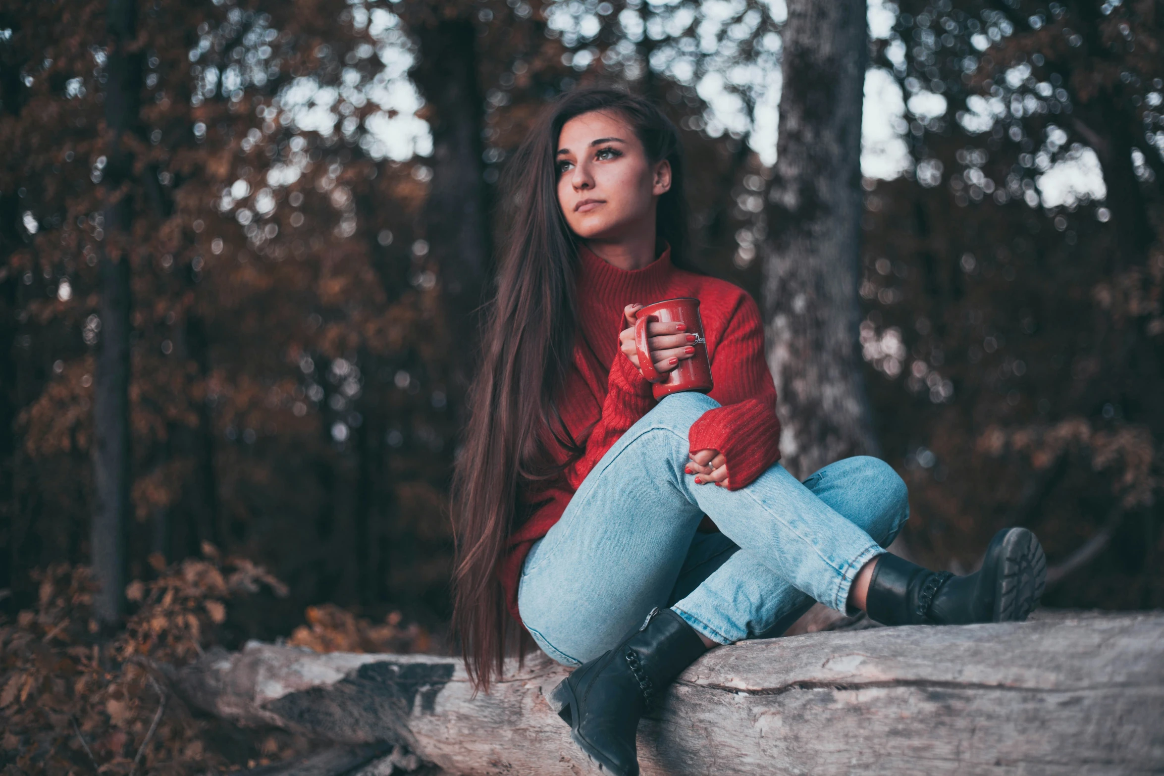 a woman is sitting down on a log in the woods