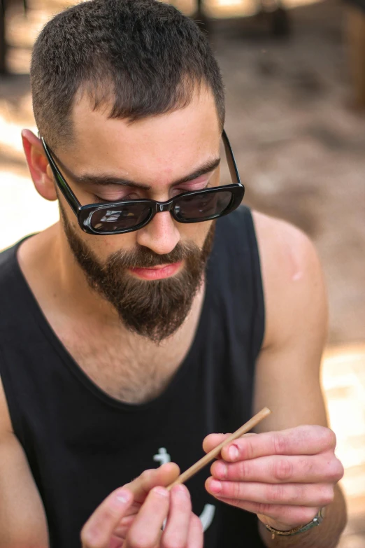 a bearded man with sunglasses on sitting outdoors with a cigar in his hand