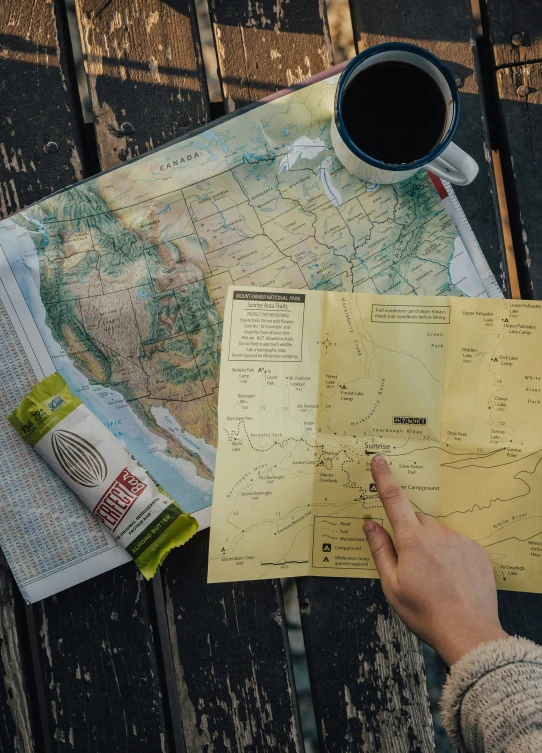 a persons hand holding a map in front of some papers and a cup of coffee