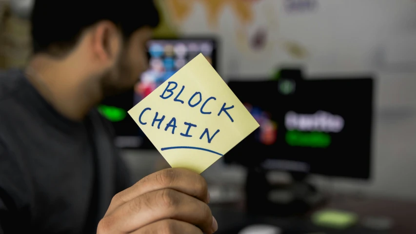 a man holding a sticky note that says block chain