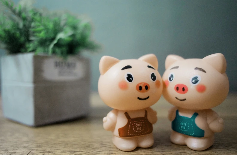 two small pig figurines on a table near a plant