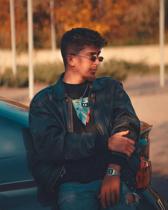 a man with his arms crossed sitting on the hood of a car