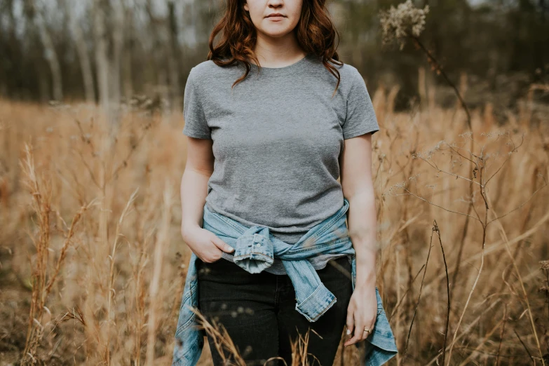 a woman in a grey t - shirt standing among brown grass