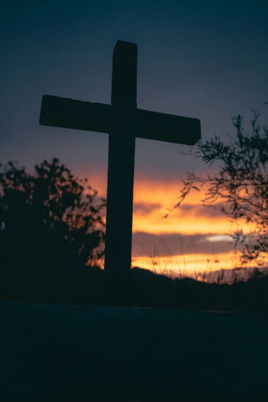 a wooden cross on top of a hill near the sunset