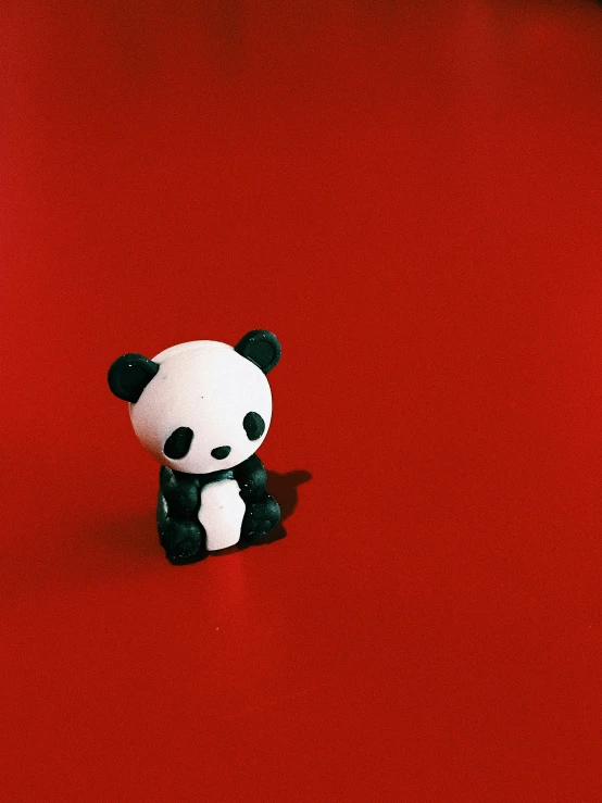 a small white panda bear with black ears sitting on a red surface