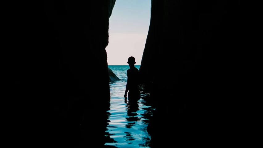 silhouette of a person standing in the ocean between two rocks