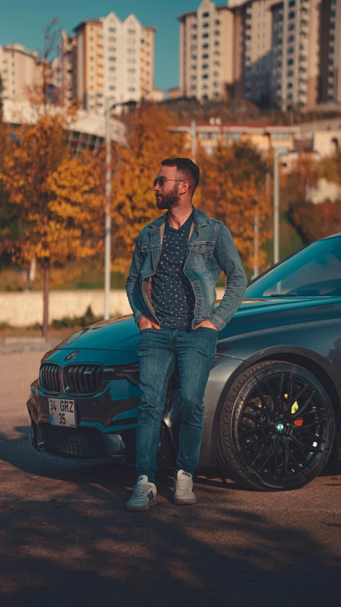 a young man standing in front of a blue bmw