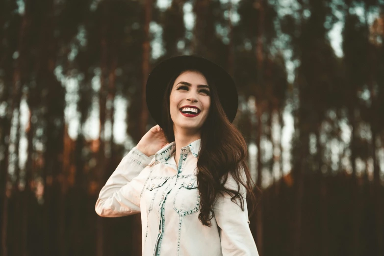 smiling woman in a hat in front of pine trees