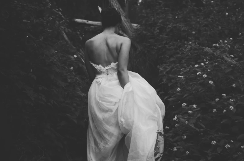 a woman in a white dress looking down at flowers