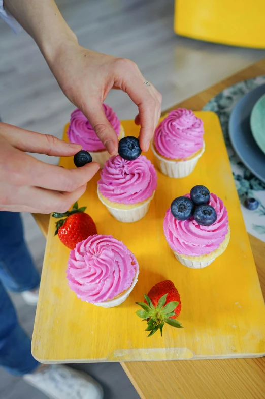 someone adding frosting on cupcakes with fresh blueberries and strawberries