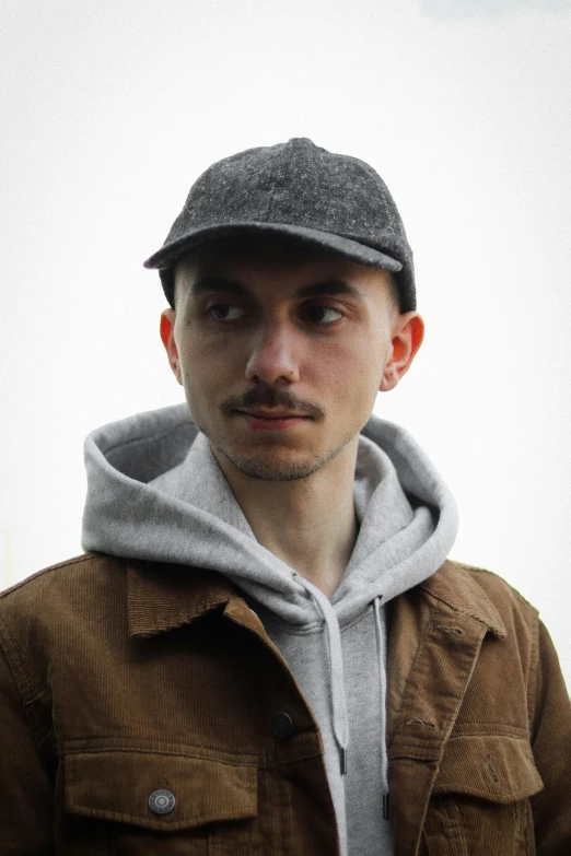 a young man wearing a hat standing against the sky