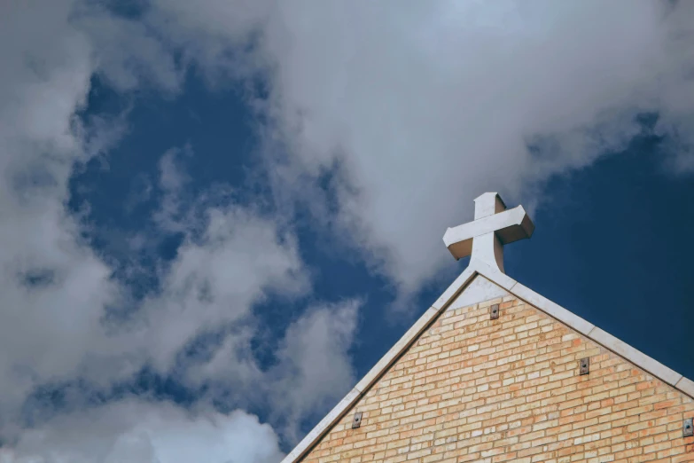 cross on top of brick church roof against cloudy blue sky