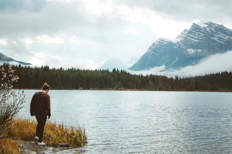 a woman is standing in a lake next to the mountains