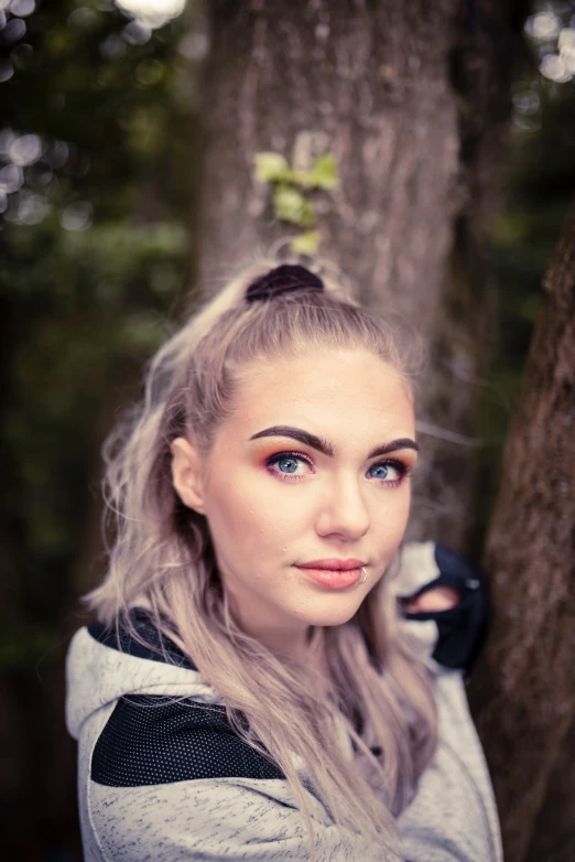 the girl stands under a tree with long blond hair