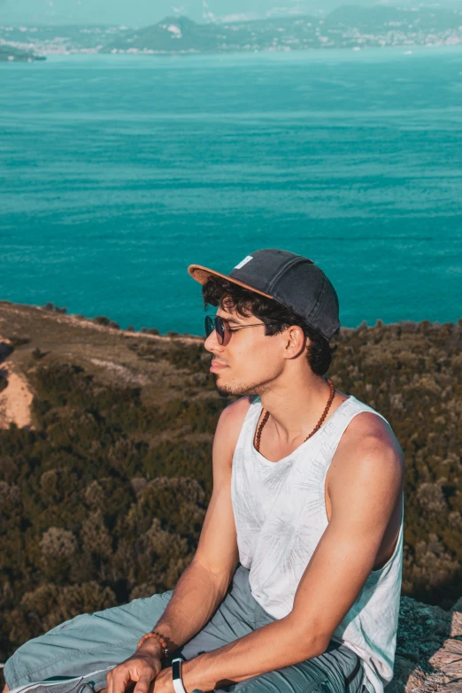 a young man wearing sunglasses and hat sitting on rocks