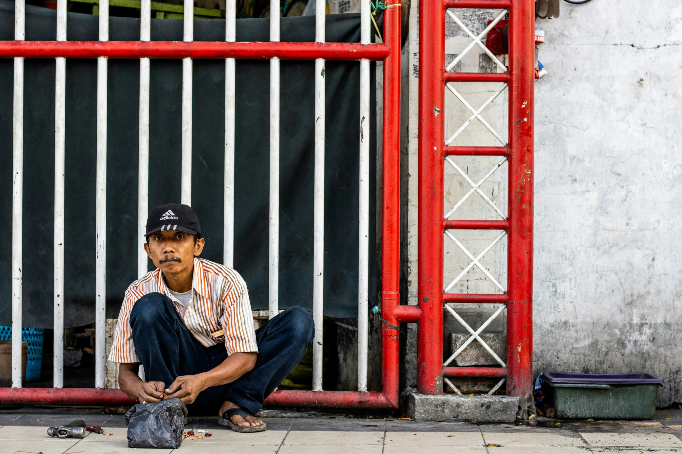 a man sitting on a street corner near a metal fence