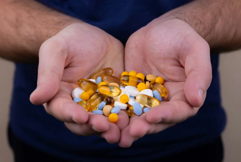 a man holding out two hands filled with prescription pills