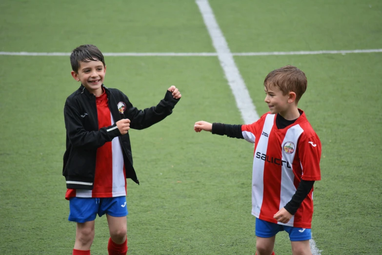 two little s standing on a soccer field pointing to each other