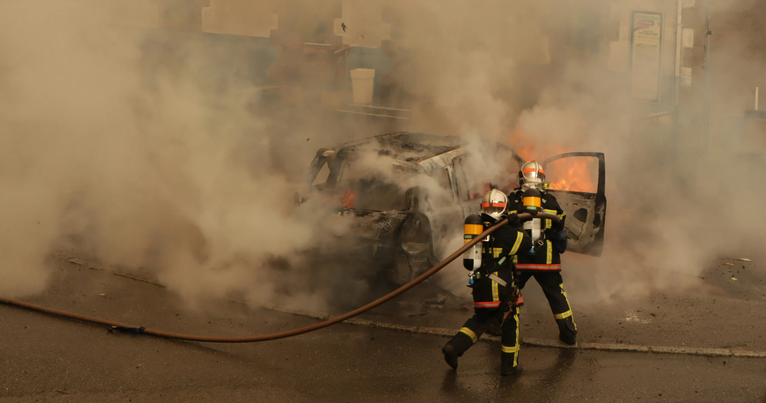 two firefighters walking with hoses attached to car