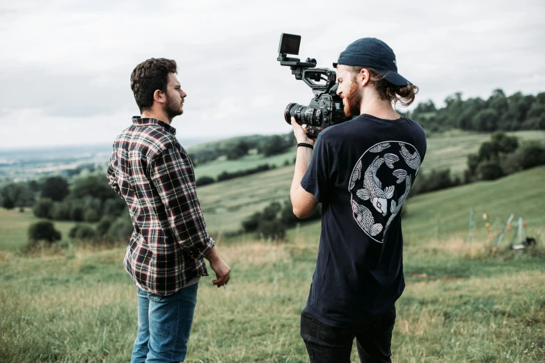 two men standing in a grassy field while holding a camera