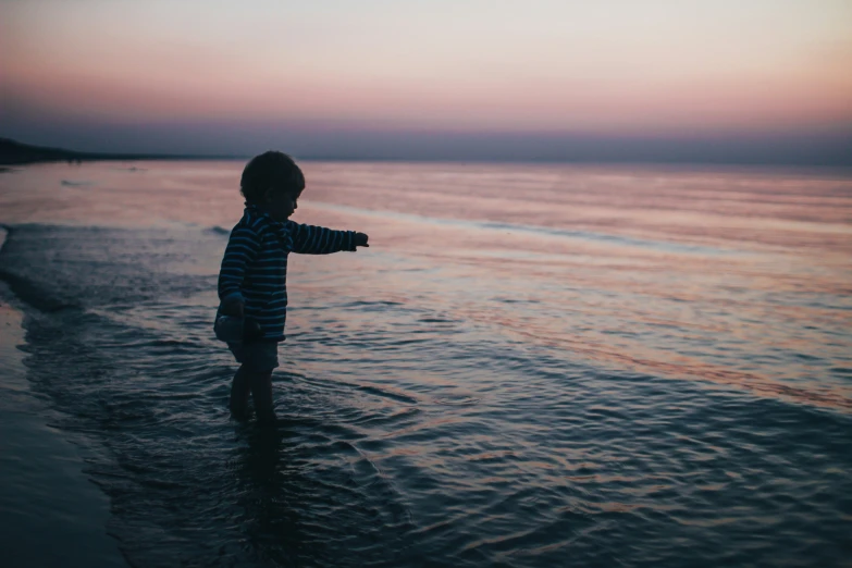 a little boy in the ocean waves towards the sunset