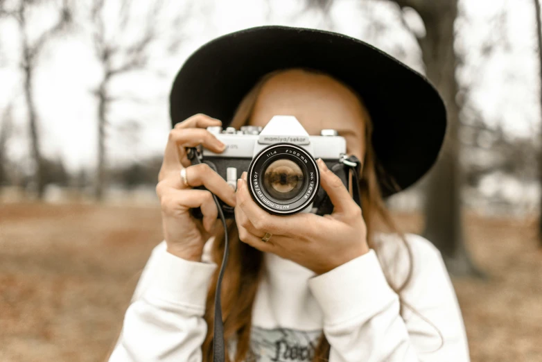 a girl wearing a hat holding up a camera