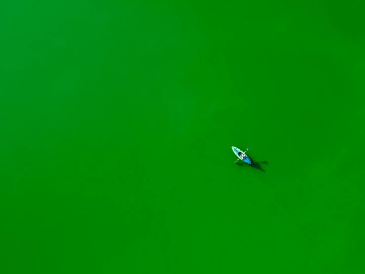 an overhead view of a man with a surfboard in the green water