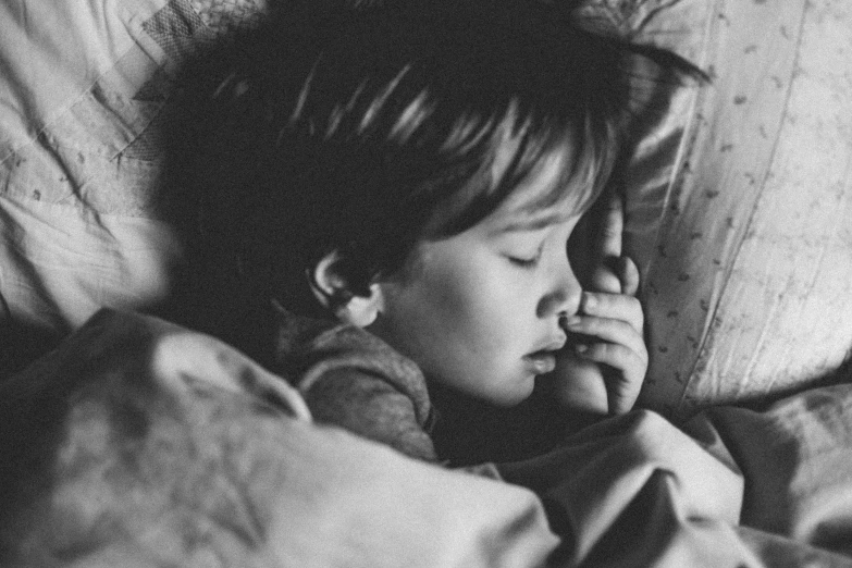 a boy in bed talking on a phone while holding his hand to his ear