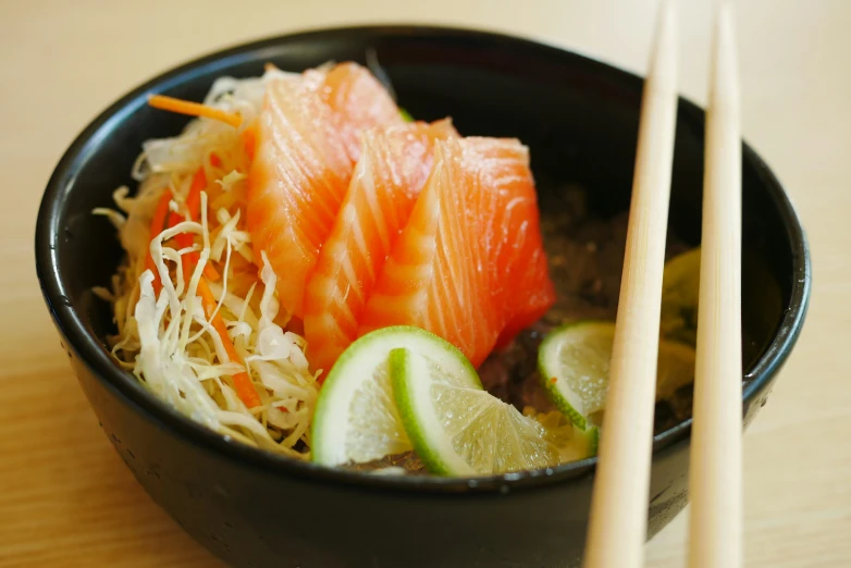 this asian noodle bowl is topped with salmon, cucumber, and green onions