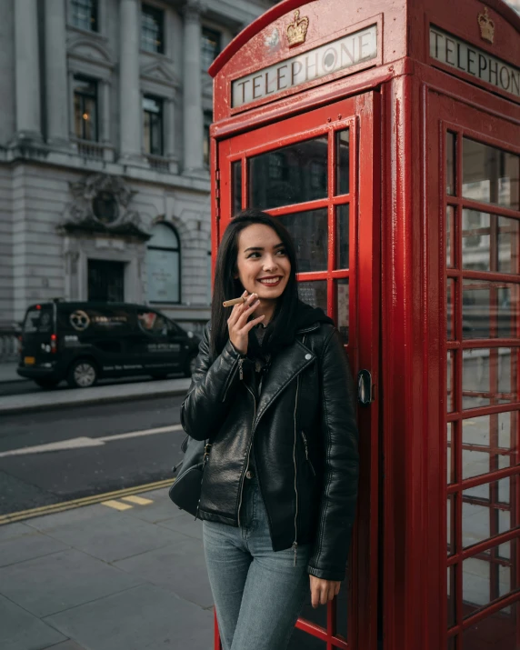 woman leaning against a red phone booth and smiling