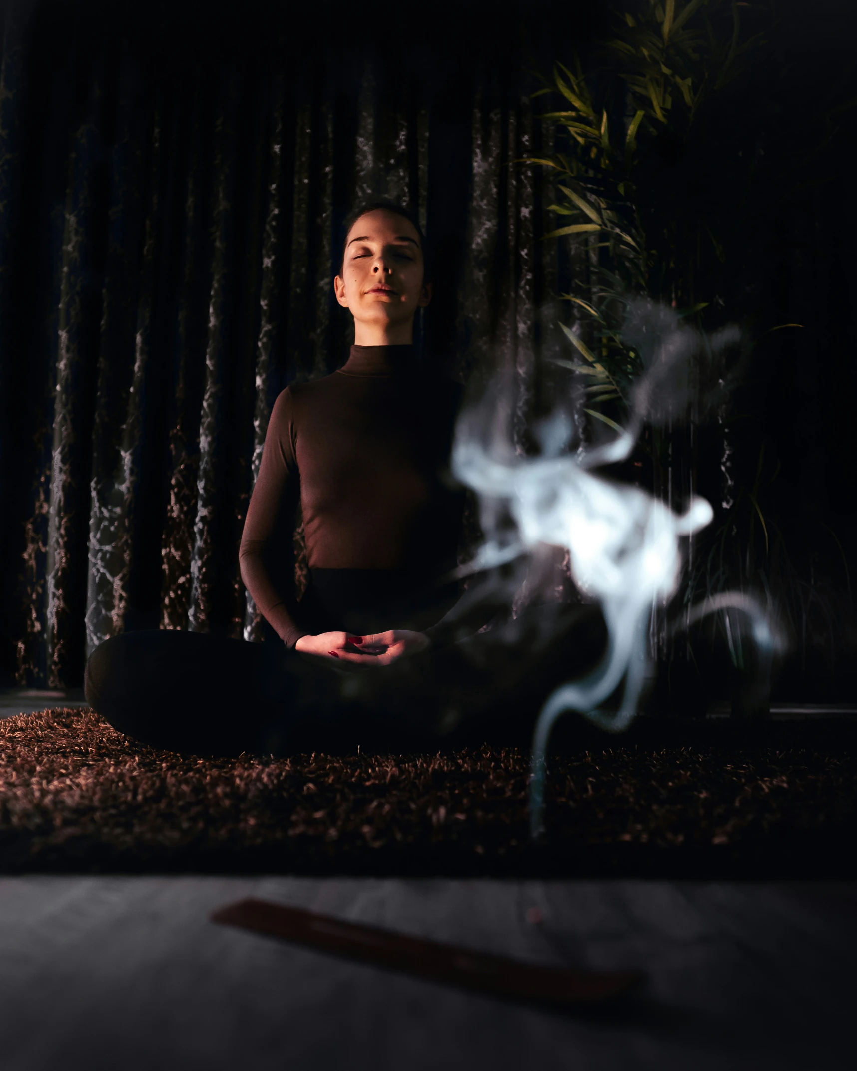 a woman in the dark sits on the floor, with smoke coming out from her legs