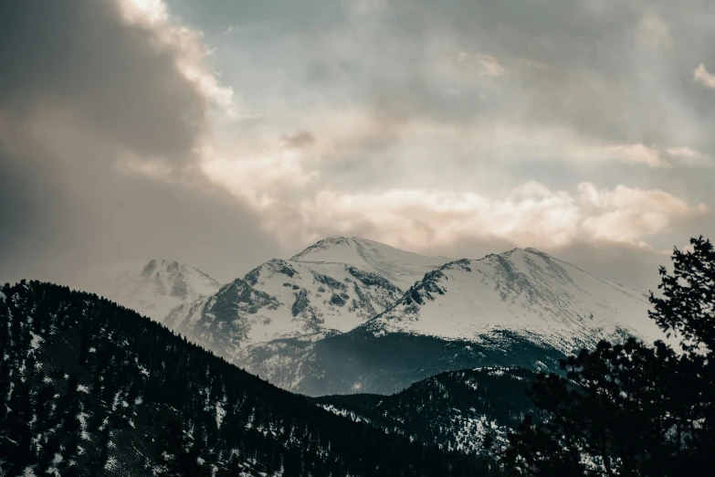 the sun shines through clouds over snow capped mountains