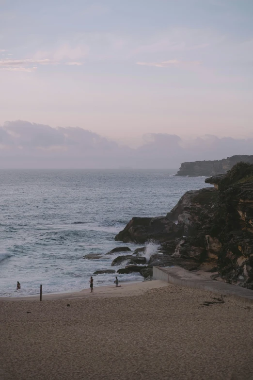 people walk on the shore of a beach next to the ocean