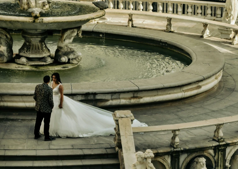 a bride and groom standing in front of a fountain