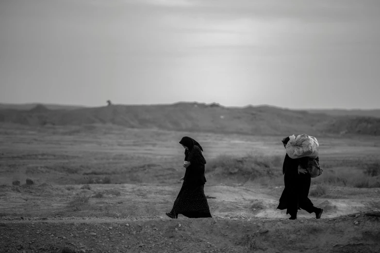 two women walking in the desert carrying large umbrellas