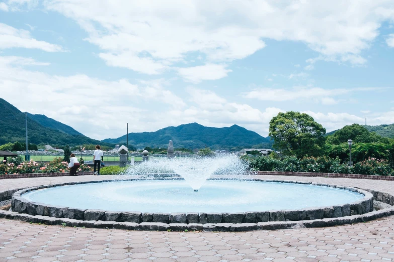 a man walking down a brick street past a large water fountain