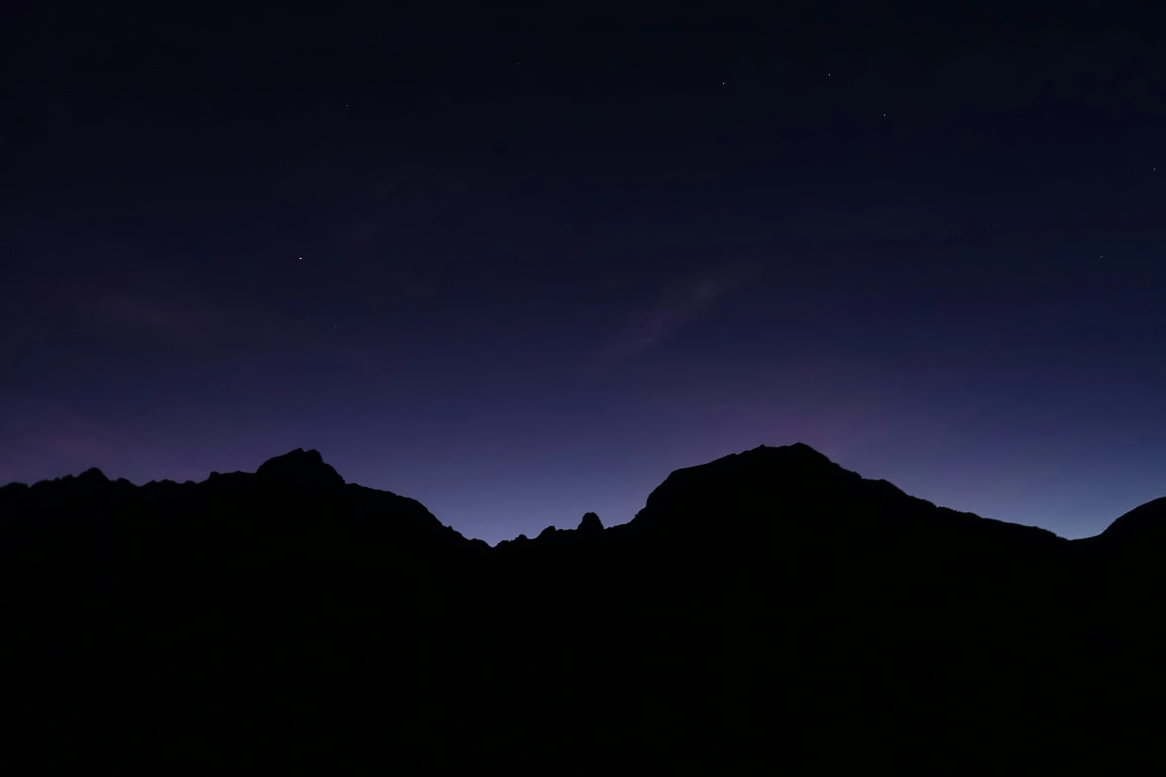 the silhouette of mountains against a purple sky