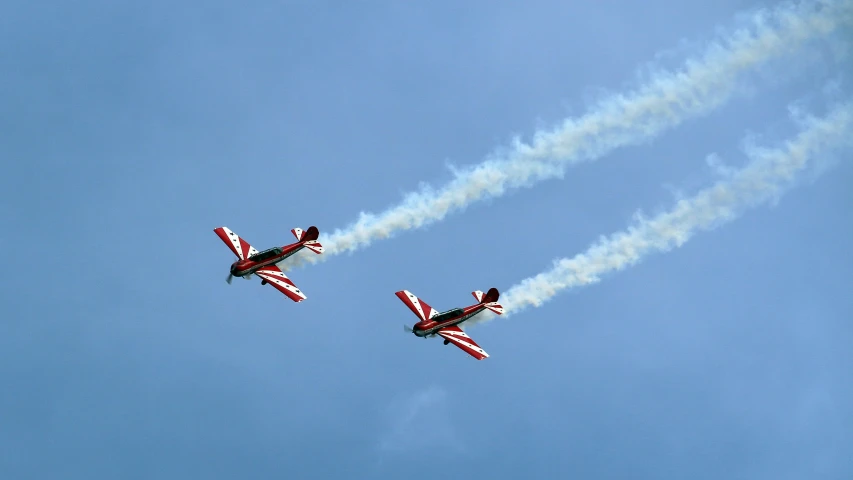 two airplanes fly in the blue sky leaving smoke behind them