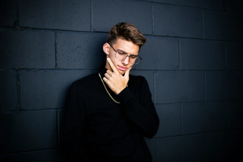 a person with glasses standing next to a black brick wall