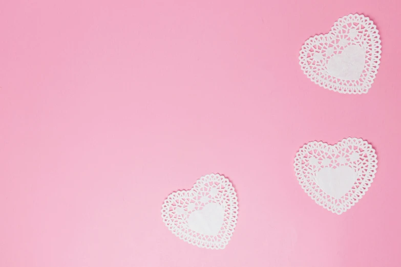 white lace hearts on pink paper laid out