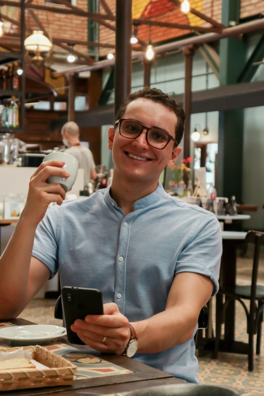 a man sitting down at a table holding up an electronic device