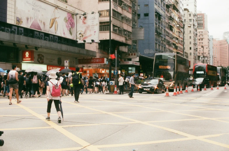 people and buses on a city street with buildings