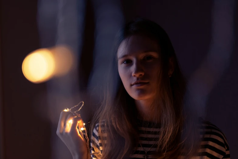 a woman holds a lit object in a darkened room