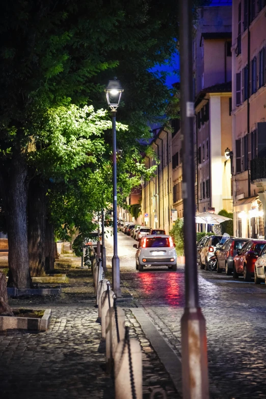 a street at night is filled with parked cars and several lamps