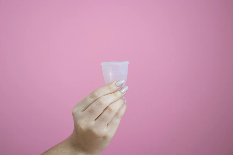 a hand holding a glass against a pink wall