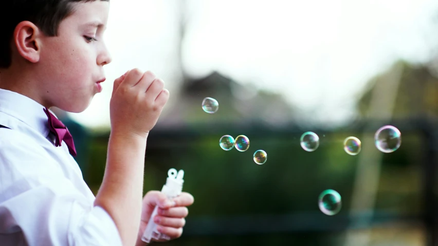 the boy in the tie is blowing soap bubbles