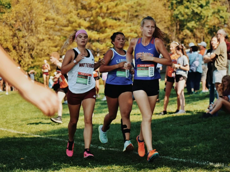 a group of women run through a grassy area