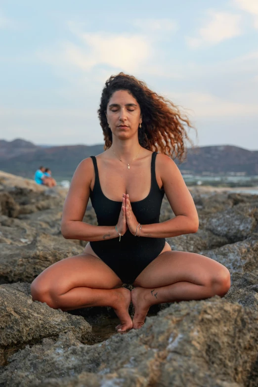 a young woman meditates while sitting on rocks at the beach