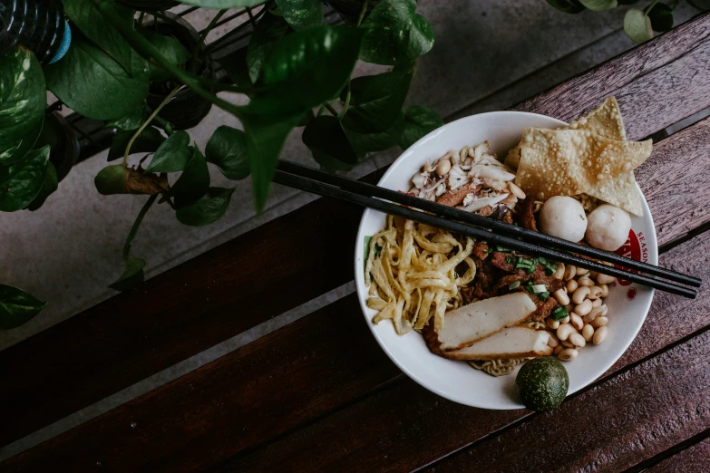 a white bowl containing noodles, meat and vegetables with chopsticks