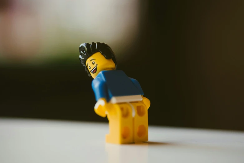 lego man with blue shirt and black hair with head tilted over white surface